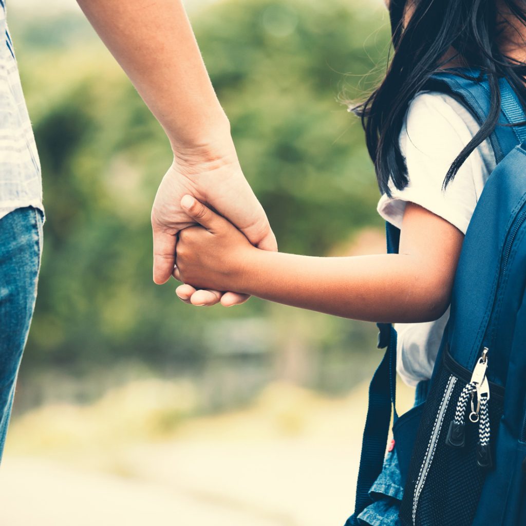 Child wearing backpack holding woman’s hand